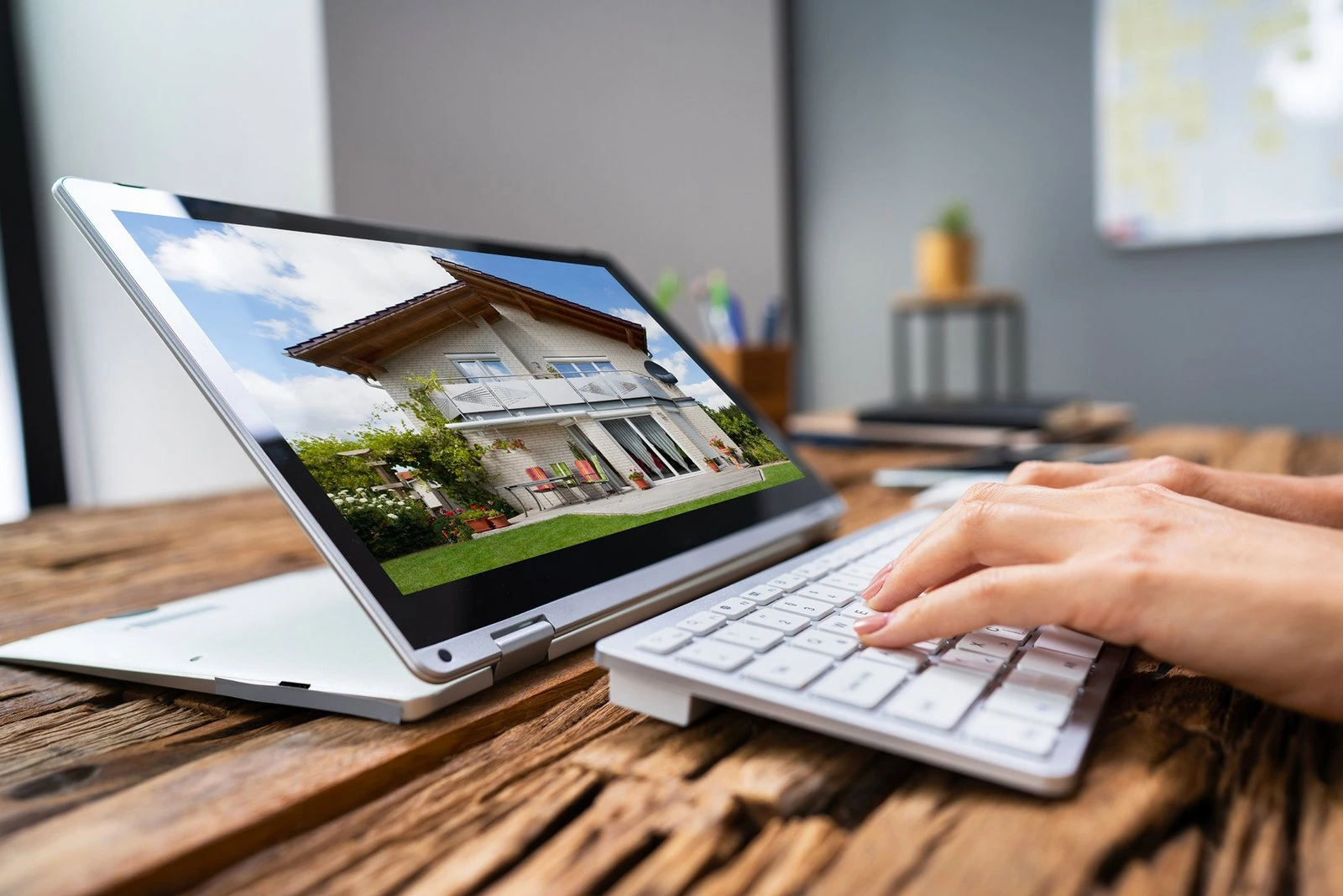 Person typing at a desk with a tablet showing a modern house image on screen