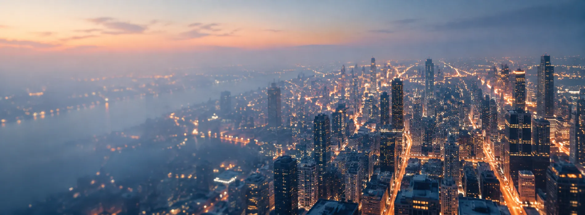 An aerial view of a dense city at blue hour, its streets glowing with warm light