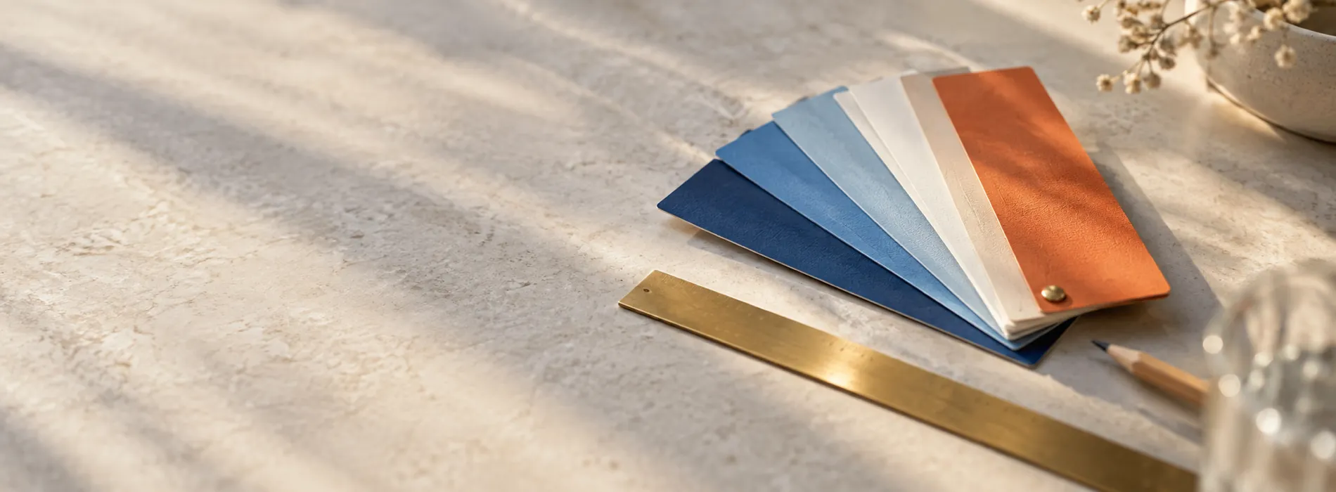 A fan of blue, cream and orange colour swatches with a brass ruler and pencil on stone