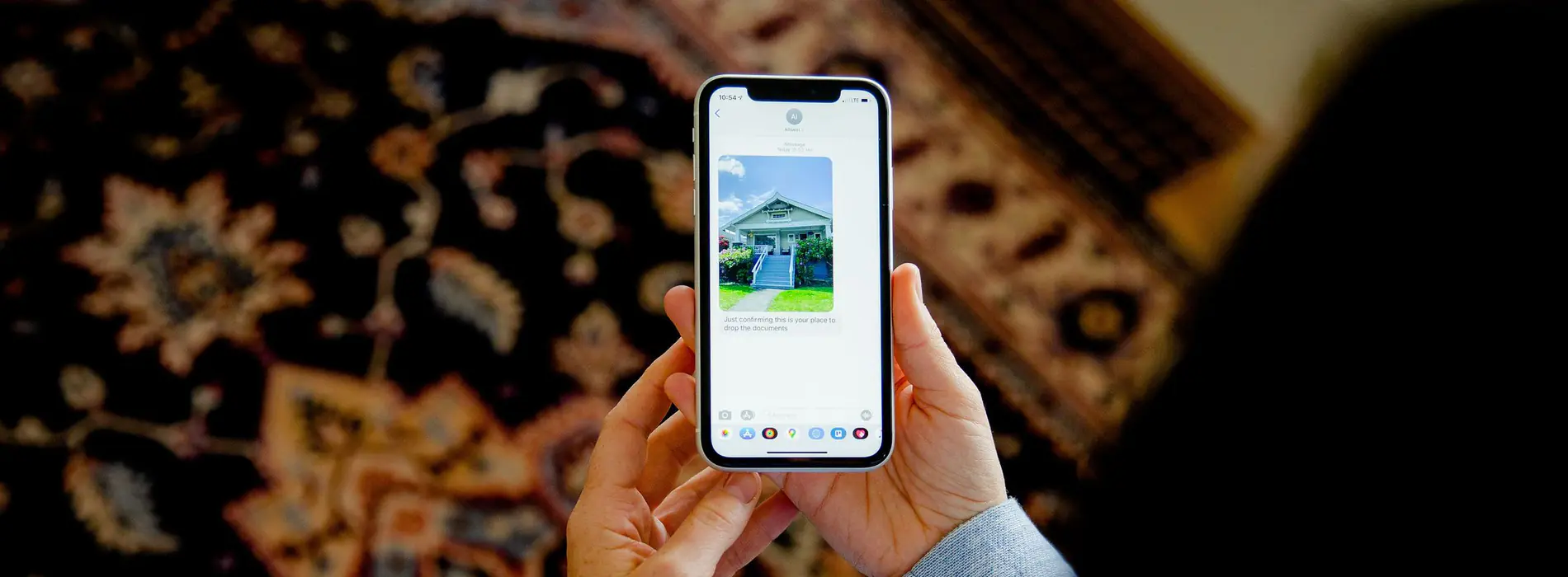 Hands holding a phone that shows a photo of a blue house with white steps, above a patterned rug