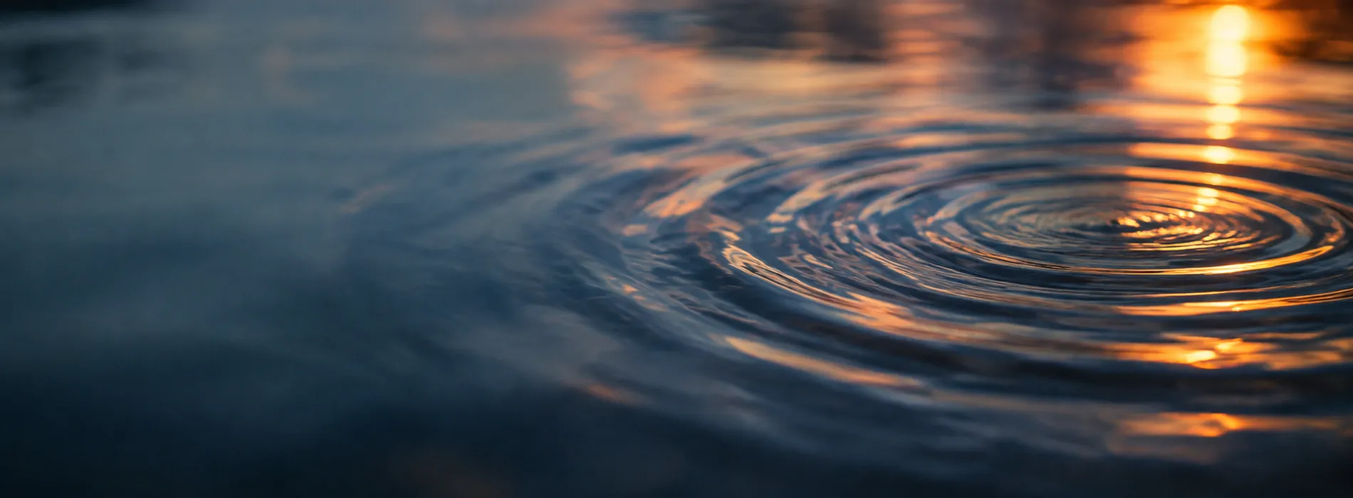 Ripples spreading across dark water, catching blue and orange light