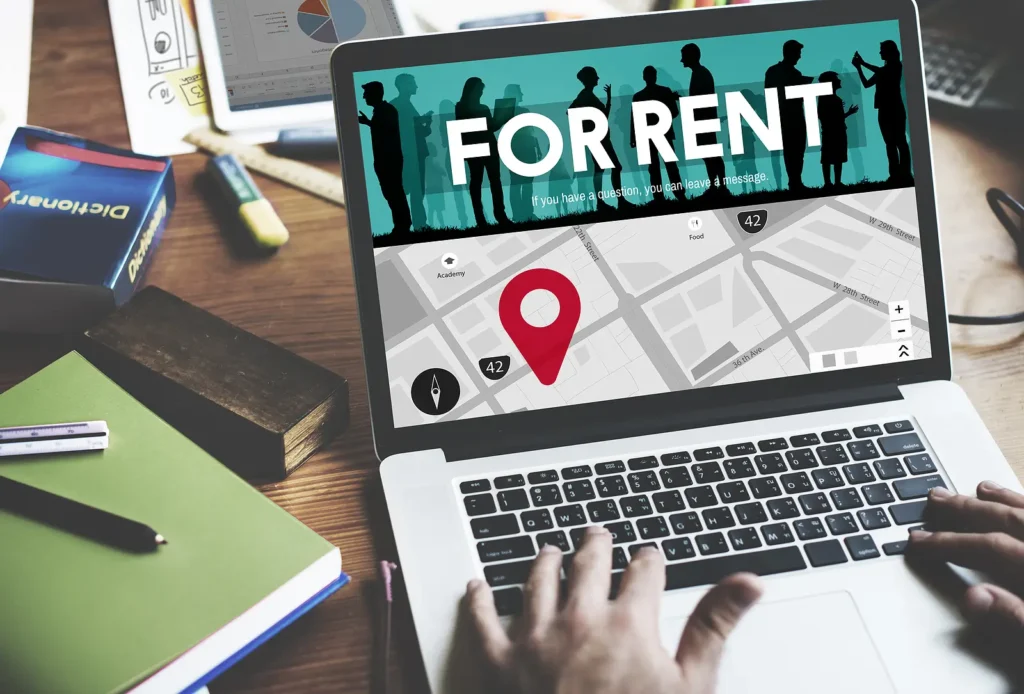 Laptop screen shows a 'FOR RENT' banner over a city map with a red location pin and silhouettes in the banner area.