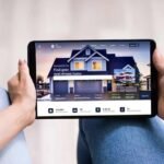 Property-Management-Software-Development-for-Real-Estate-1 - Kihan Marketing Two people sit with a tablet displaying a real estate website featuring a large house image and search options nearby