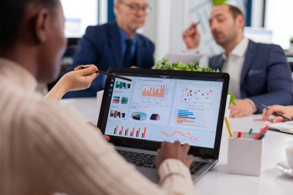 Business colleagues discuss data in a meeting, with a laptop showing charts and graphs on the screen.