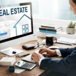 real-estate-seo-services-1 - Kihan Marketing Man in a suit typing at a desk while a real estate website loads on a desktop monitor on his left side.