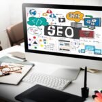 seo-search-engine-optimization-internet-digital-concept-scaled-1 - Kihan Marketing Monitor showing a colorful SEO doodle illustration on a white desk, with the word 'SEO' and related icons surrounding it.