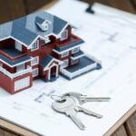 villa-house-model-key-drawing-retro-desktop-real-estate-sale-concept-scaled-1 - Kihan Marketing Model red-brick house figurine on architectural blueprints with a set of keys beside it, symbolizing real estate or home purchase