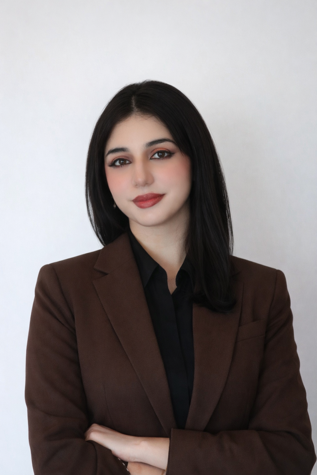 Professional head-and-shoulders portrait of a woman with shoulder-length dark hair, wearing a brown blazer over a black top, arms crossed against a light background.