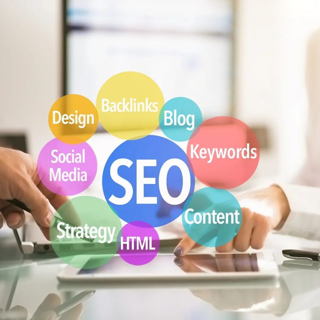 Colorful bubbles labeled with SEO terms (SEO, Design, Backlinks, Blog, Keywords, Content, HTML, Strategy, Social Media) arranged around a central SEO on a glass desk surface.