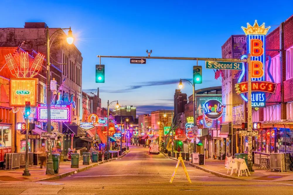 Nighttime street scene of a neon-lit entertainment district with colorful signs and storefronts outside bars and clubs.