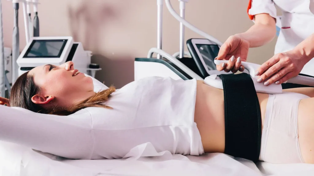 Woman lying on a clinic bed during a body contouring treatment with a handheld device applied to her abdomen/torso area