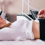 668ce9def91093c94779f481_image3-1 - Kihan Marketing Woman lying on a clinic bed during a body contouring treatment with a handheld device applied to her abdomen/torso area