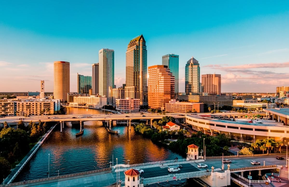 City skyline at sunset with tall glass skyscrapers, a river, and multiple bridges crossing a downtown canal due to waterway traffic.