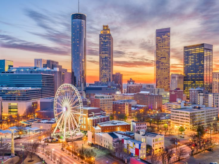 Downtown skyline at sunset with a lit Ferris wheel in the foreground.