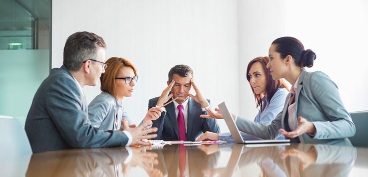 9b62ef87d199dcc595e05395a8f2fdff - Kihan Marketing - Kihan Marketing Five professionals in a boardroom around a glass table; the center man holds his temples as colleagues discuss surrounding him.