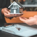 New-Seattle-Rent-Cap-in-2026-1024x683 - Kihan Marketing Hands exchanging a small house model over a signed contract on a table, with a key nearby (real estate transaction).
