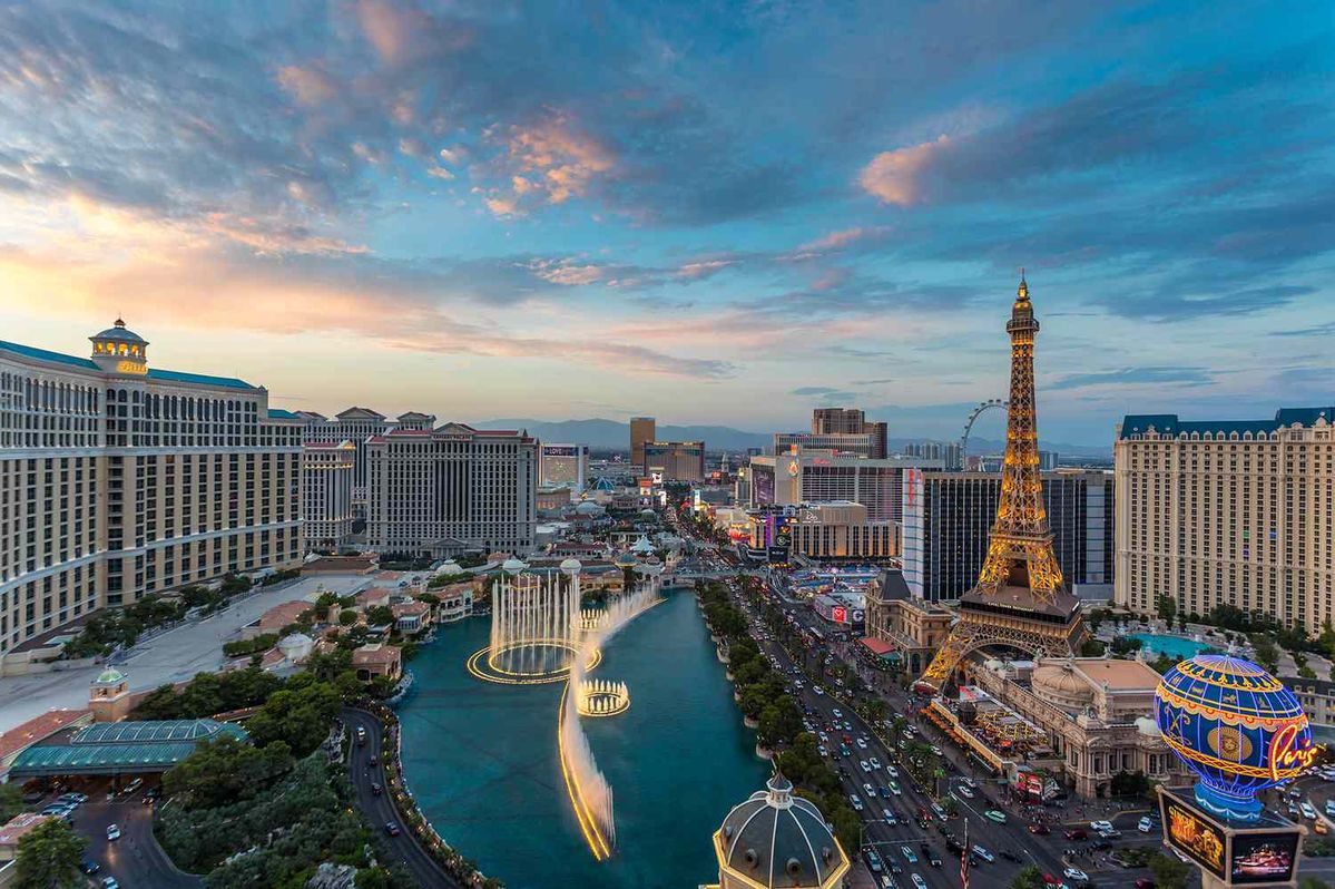 Aerial view of the Las Vegas Strip at sunset with the Bellagio fountain lake, Paris Las Vegas Eiffel Tower replica, and surrounding hotel casinos.