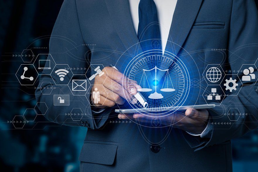 Businessperson in a dark suit holds a tablet with holographic legal and tech icons, including scales of justice, projected in blue light
