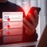 642aa6ac83fdf5af0293634117678b25 - Kihan Marketing Person holds a smartphone with a red glow while viewing multiple message notifications with warning icons on screen