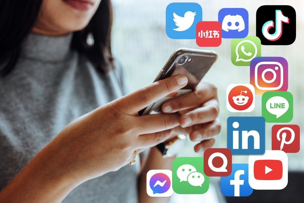 Person holding a smartphone with colorful social media icons floating around, representing social networking on mobile devices.