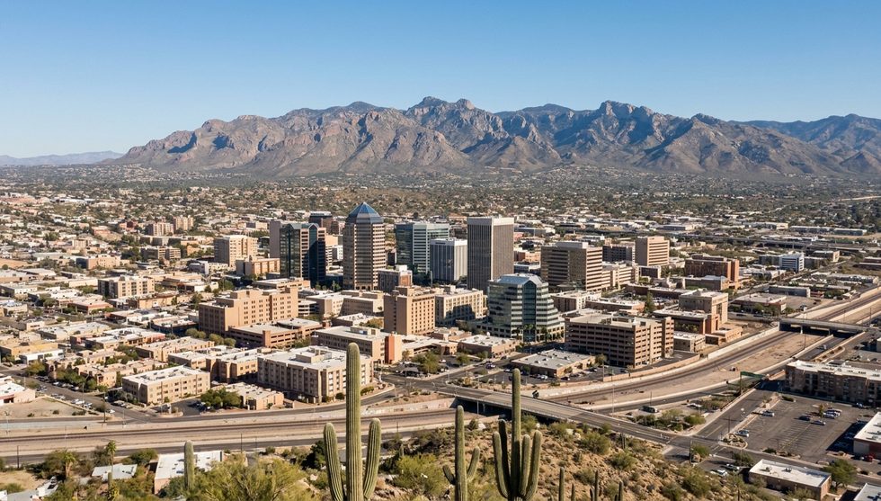 A desert city skyline with high-rise buildings, highways, and distant mountains on the horizon.