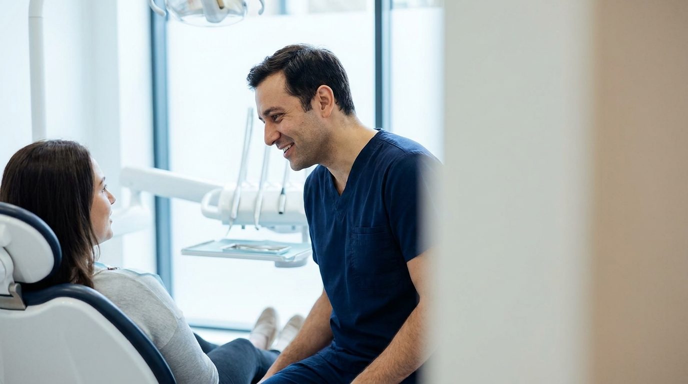 A dentist in scrubs talks with a patient in a bright modern surgery